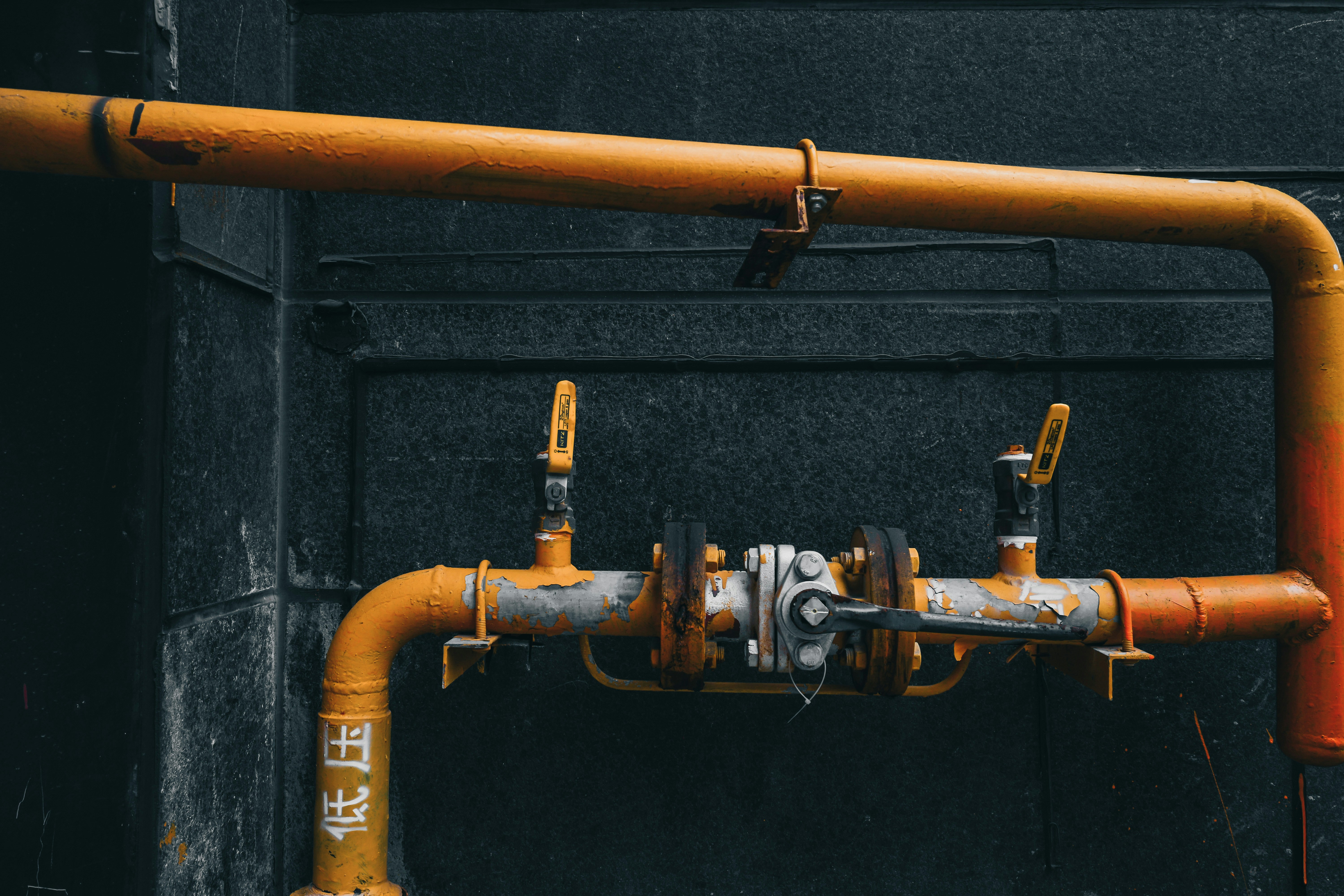 Industrial orange pipes with valves against a dark wall