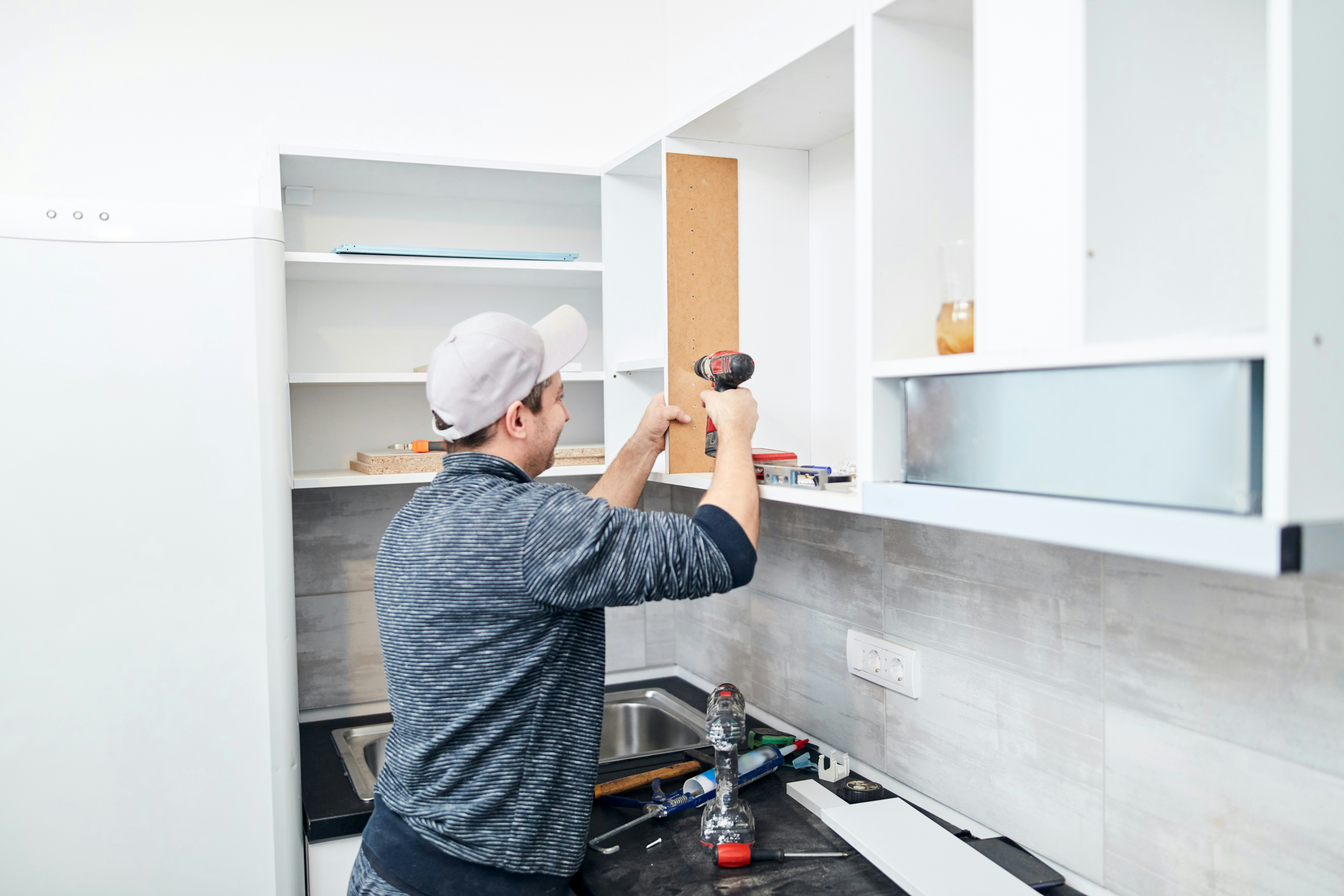Worker installing kitchen cabinets with a drill