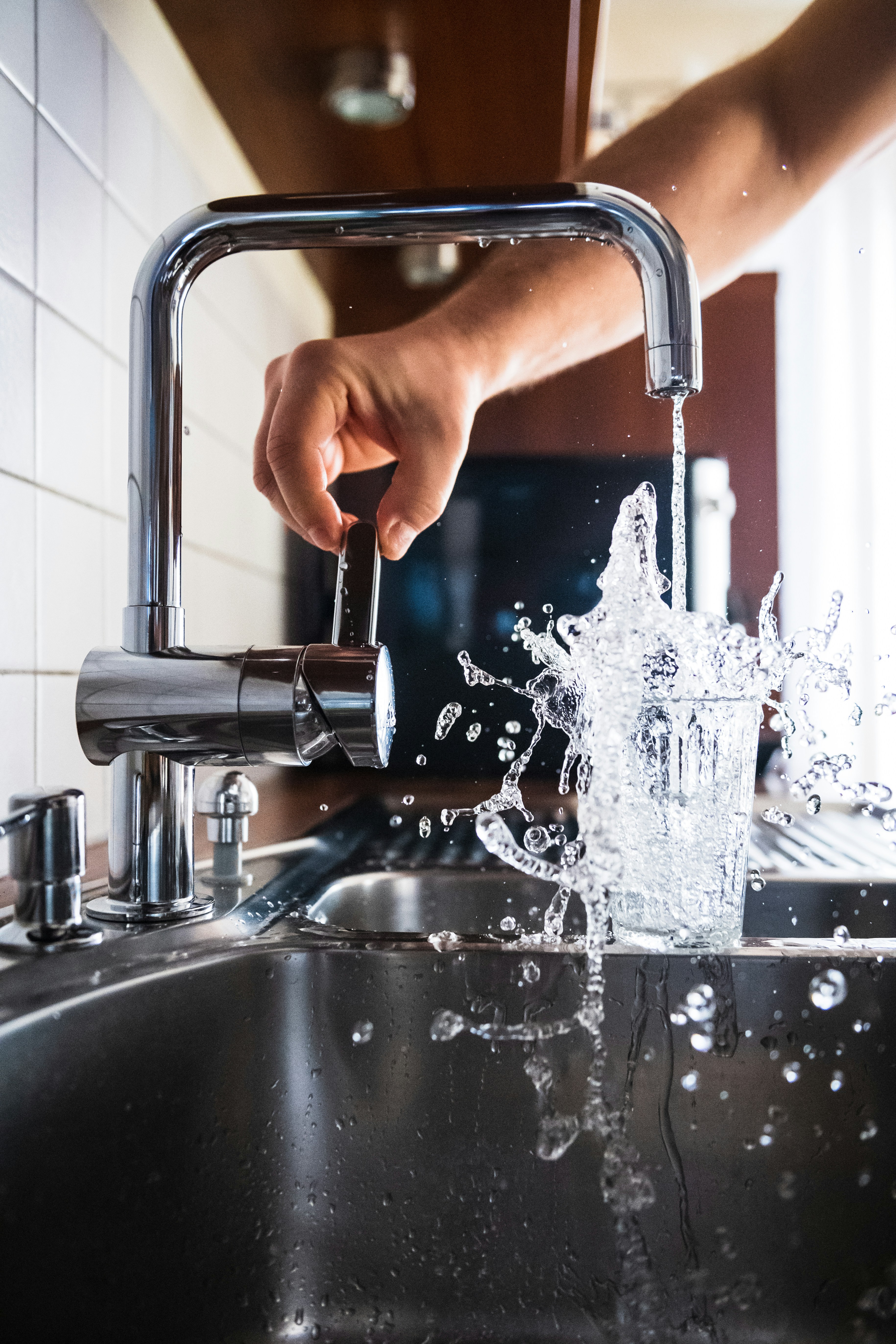 Hand turning on a kitchen faucet with water splashing into a glass