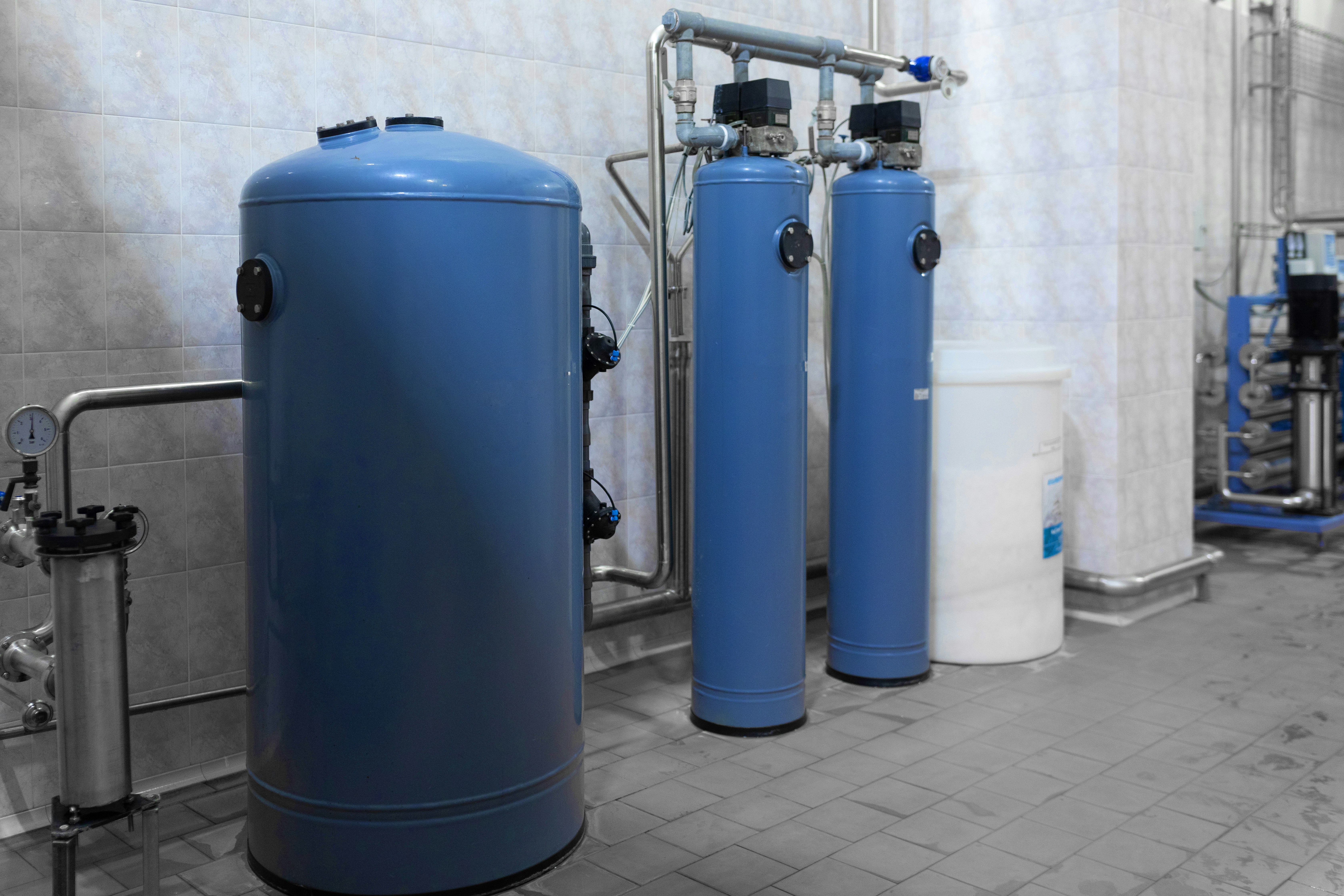 Industrial water filtration system with large blue tanks in a tiled room.