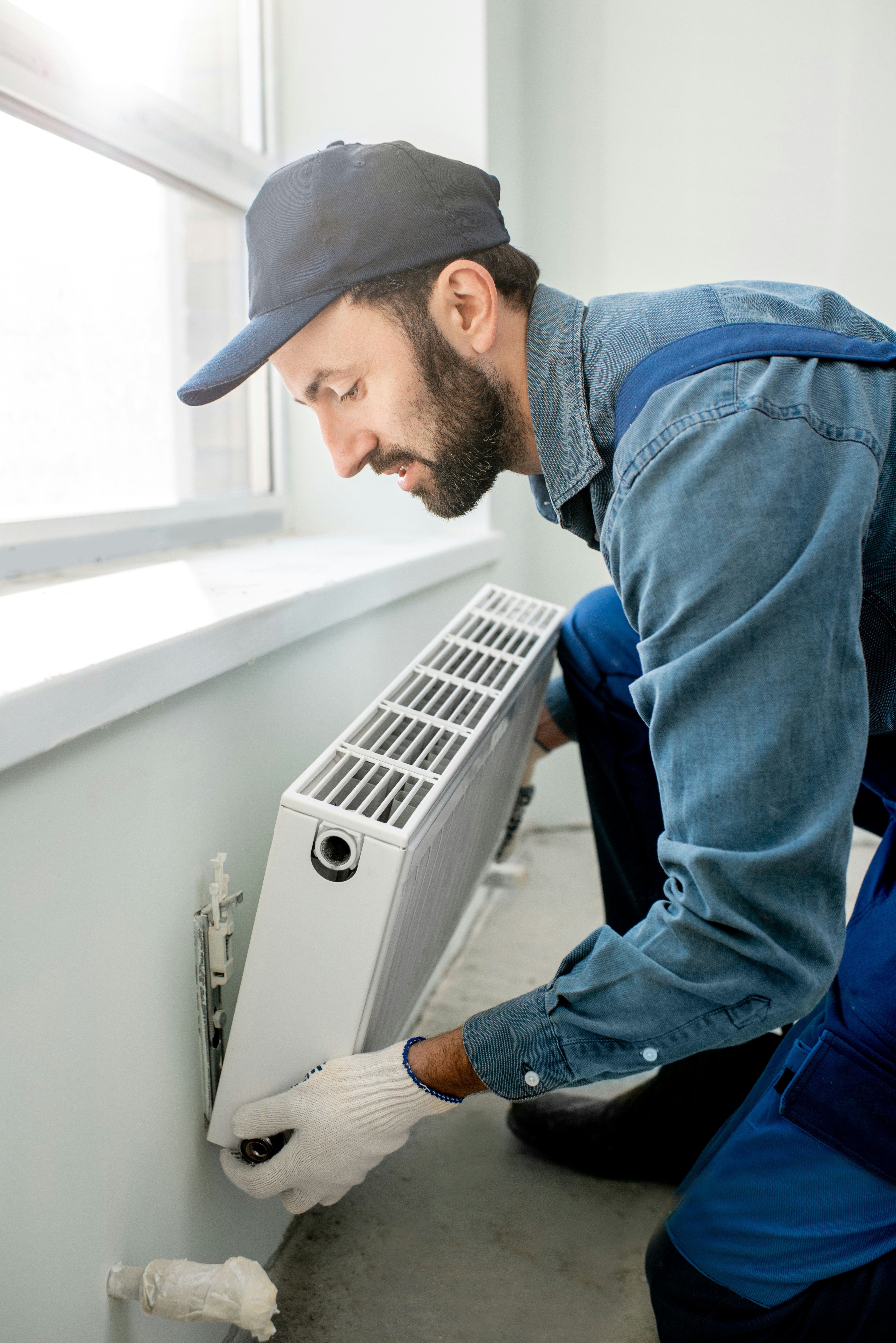 Technician installing a radiator under a window in a residential setting.