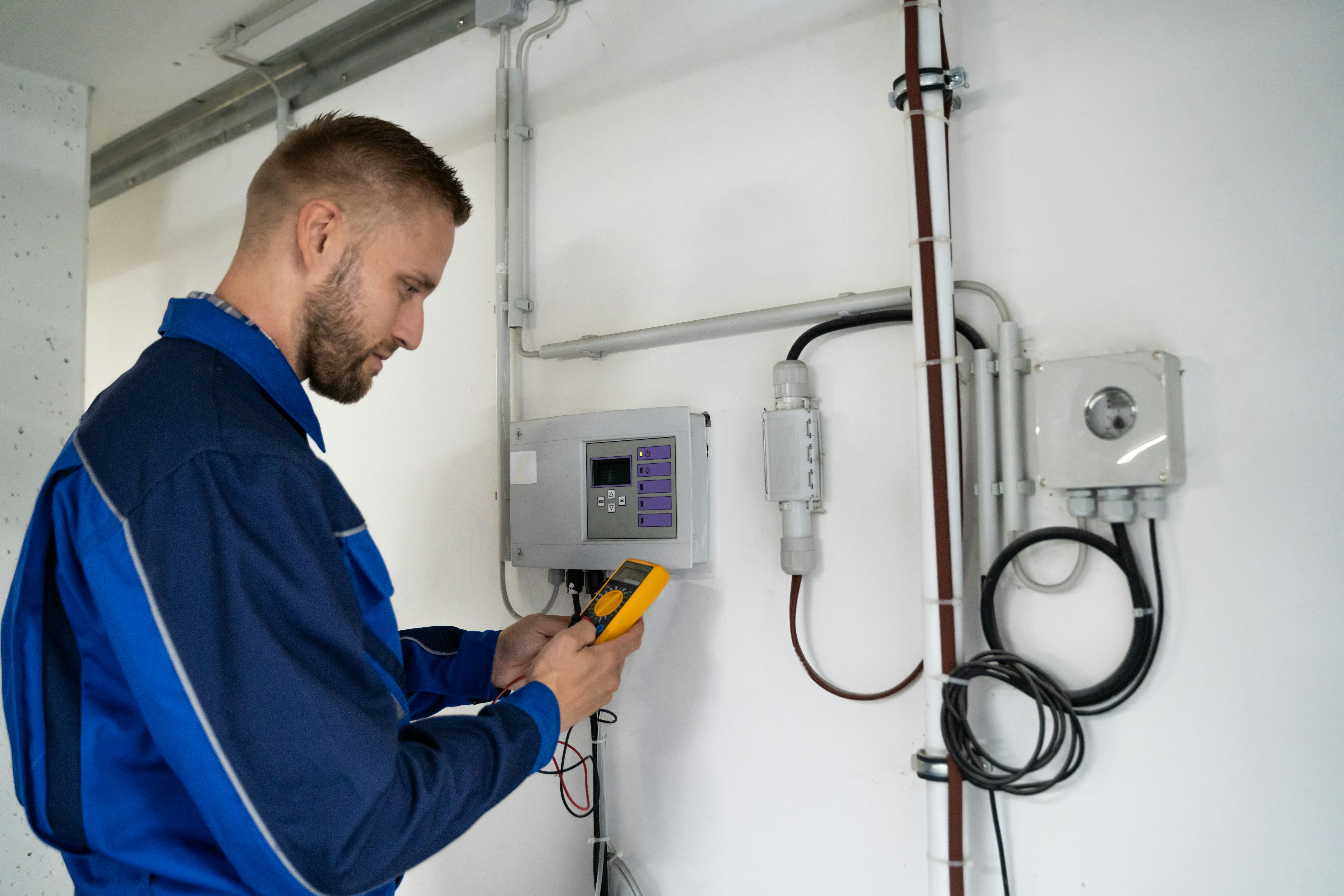 Technician in blue uniform using a multimeter on electrical panel