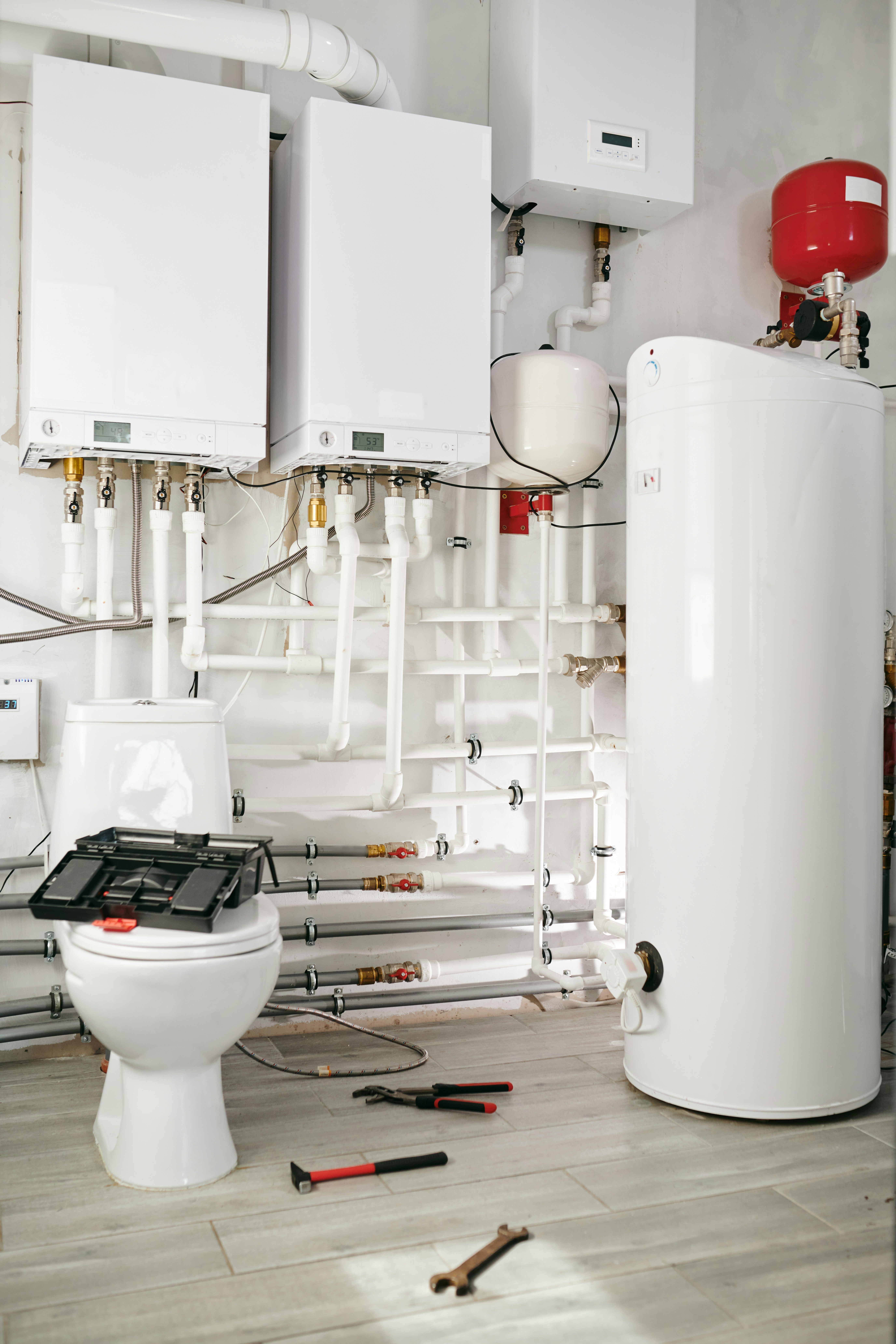 Plumbing tools and equipment in a utility room with water heaters and pipes.